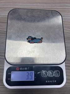 Détail d'une épinglette en émail de teckel mignon pesant 3,9 grammes sur une balance digitale