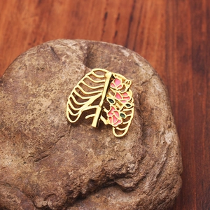 Détail d'une broche cage thoracique dorée avec fleurs en émail rose sur une pierre brute
