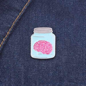 Détail du pin's émaillé en forme de cerveau dans un flacon sur tissu en jean bleu