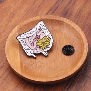 Broche en émail montrant l'anatomie intestinale avec fleur de lys et texte de confiance