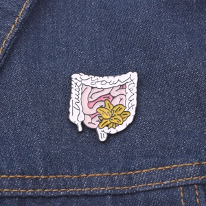 Vue macro d'un pin's émaillé anatomique avec texte Trust Your Gut sur veste en jean