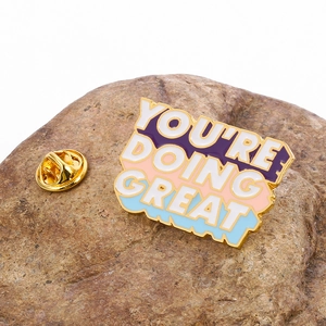 Macro shot of You're Doing Great enamel pin on a stone with golden butterfly clasp