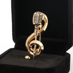 Macro detail of gold microphone and treble clef music brooch on black velvet background