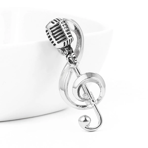 Detail shot of vintage silver microphone and treble clef music brooch on white porcelain