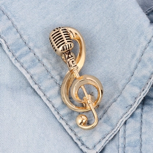 Detail of vintage gold microphone and music note brooch on light blue denim fabric
