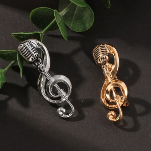 Vintage microphone and musical note brooches in gold and silver finish on black background