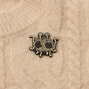 Detailed view of the Flying Spaghetti Monster enamel brooch pinned on a beige sweater