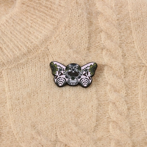 Close-up of enamel moth skull brooch with floral details on a beige knit sweater