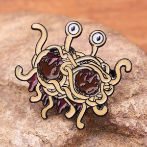 Flying Spaghetti Monster enamel pin with googly eyes and meatballs on natural stone