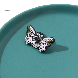 Detailed macro view of moth sugar skull enamel brooch on a blue ceramic jewelry display