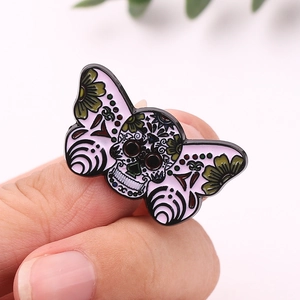 Detail view of a moth skull enamel pin in pink being held to show size and texture