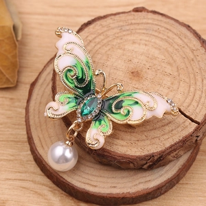 Close-up of enamel butterfly brooch with green crystal and hanging pearl detail