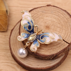 Detailed close-up of a butterfly brooch with crystal wings and a dangling white pearl