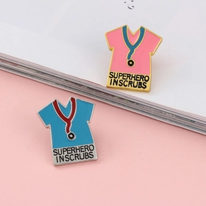 Detail of pink and blue enamel pins featuring medical scrubs and superhero text