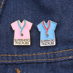 Detail of enamel stethoscope pins with Superhero In Scrubs text on denim fabric