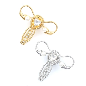 Makroaufnahme der Gold- und Silber-Uterus-Pins mit Herz-Zirkon und Perlen-Details