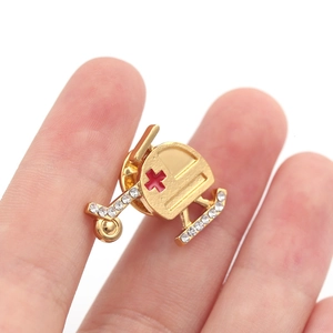 Close-up of golden helicopter brooch with red cross and rhinestones shown on finger