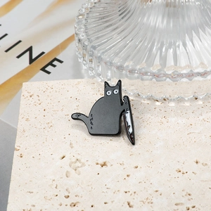 Detail of a black killer cat enamel pin with a bloodied knife on beige stone texture