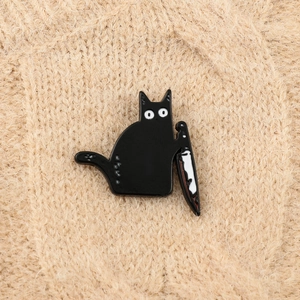 Macro detail of cartoon killer black cat enamel pin holding a knife on a warm sweater