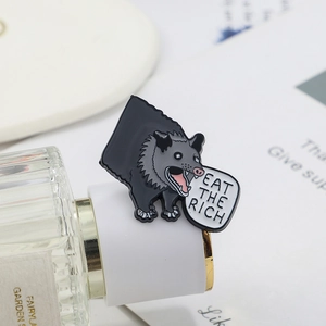 Macro shot of Inosuke enamel pin with Eat The Rich slogan on a stylish perfume bottle