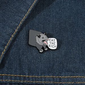 Enamel pin featuring a screaming opossum and Eat The Rich text on blue denim jacket