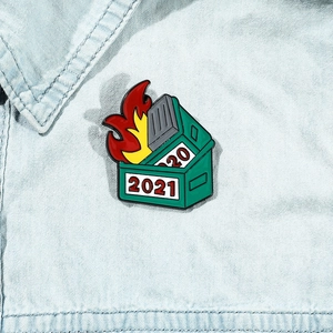 Macro detail of Dumpster Fire enamel pin with 2021 and 2020 dates on denim jacket