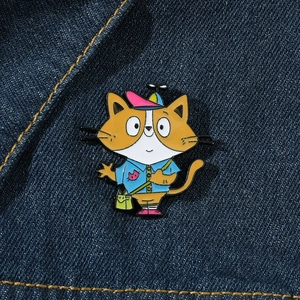 Close-up of a cartoon cat enamel pin with a propeller hat on blue denim background