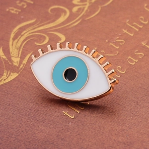 Macro detail of a rose gold evil eye enamel pin with blue eye and eyelash design