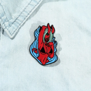 Detail of red cartoon demon enamel pin with blue hair pinned on light denim fabric