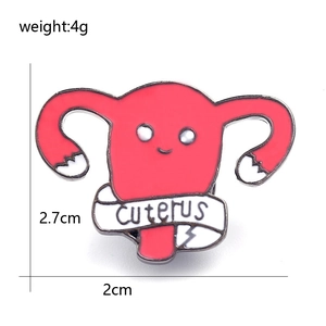 Détail macro d'une broche utérus en émail rouge avec visage cartoon et bannière cuterus