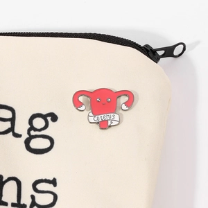 Broche utérus en émail rose avec ruban Cuterus sur un sac en toile de couleur crème