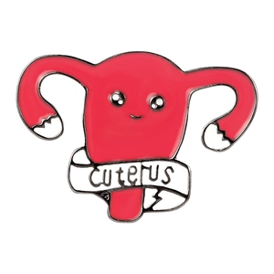 Broche utérus rose en émail avec slogan CUTERUS sur un ruban blanc, style dessin animé