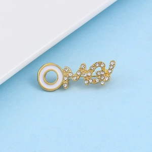 Macro-detail van de OMG-broche met pavé strass-steentjes en wit email op goud metaal
