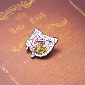 Detail of enamel organ brooch with 'Trust YOUR gut' text and a yellow lily on notebook