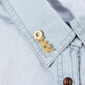 Macro-detail van de OMG gouden speld met micro-strass en wit email op denim