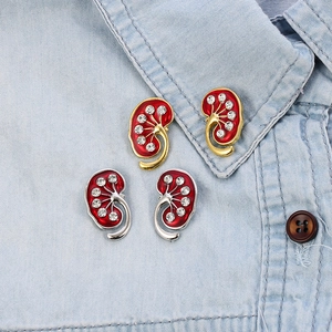 Detail of anatomical kidney brooch with red enamel and crystals on denim fabric