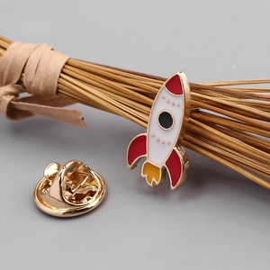 Macro shot of colorful rocket enamel pin with metal butterfly clutch on grey background