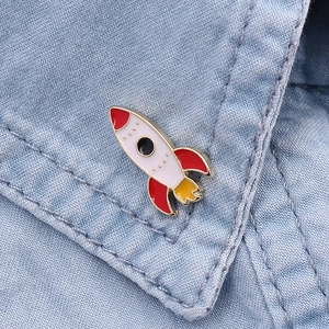 Close-up of a colorful rocket enamel pin with golden edges on blue denim fabric