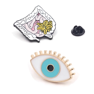 Enamel pins featuring evil eye design and anatomical organ with yellow floral accents