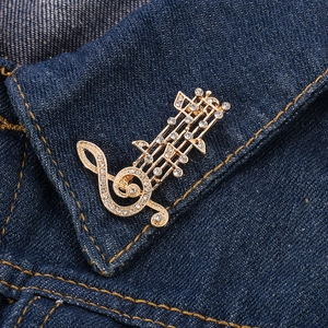 Detail shot of a crystal-studded golden musical note brooch on denim fabric