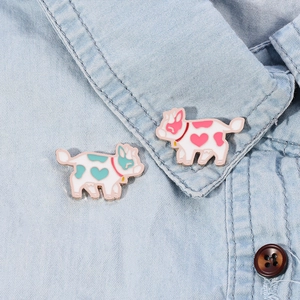 Detail of pink and blue enamel flying cow brooches on a light blue denim shirt collar
