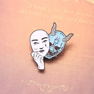 Macro detail of Oni and Hannya mask enamel pin on a book for backpack accessory decor