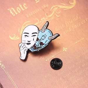 Artistic Japanese Hannya and Oni face enamel pin badge with a rubber clutch on a book