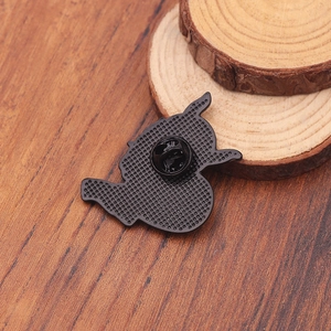 Back view of black metal character enamel pin with butterfly clutch on wood background