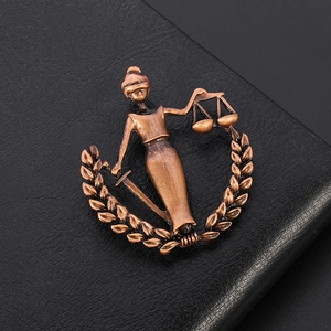 Detailed close-up of antique bronze Lady Justice brooch on a black leather background