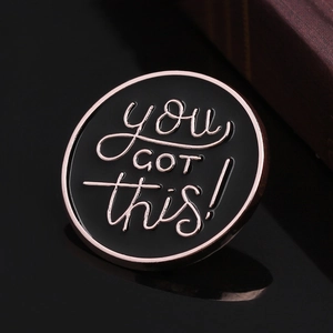 Dettaglio di una spilla tonda in smalto nero con scritta 'you got this!' e bordo oro rosa