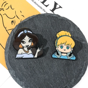Detail shot of Jasmine and Cinderella enamel pins on a black slate stand with yellow accents