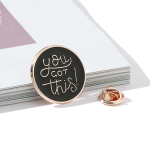 Vista macro di una spilla smaltata con testo 'you GOT this!' e chiusura a farfalla in metallo