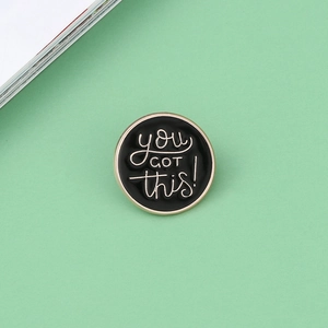 Dettaglio della spilla rotonda in smalto nero con scritta dorata 'YOU GOT THIS!'