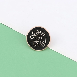 Dettaglio spilla smaltata rotonda nera con scritte motivazionali you GOT this!